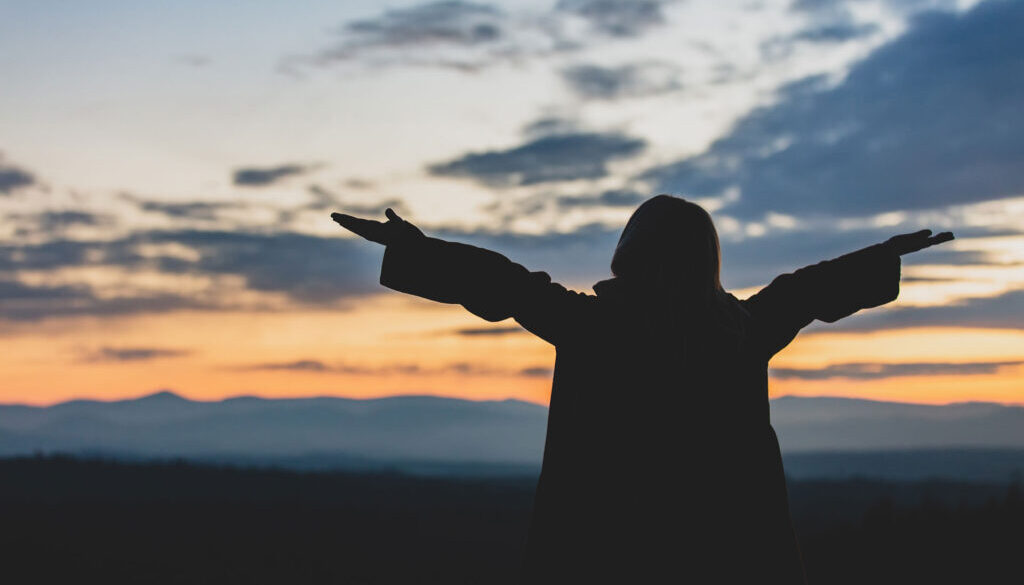 Sunset girl with arms outstretched in worship.